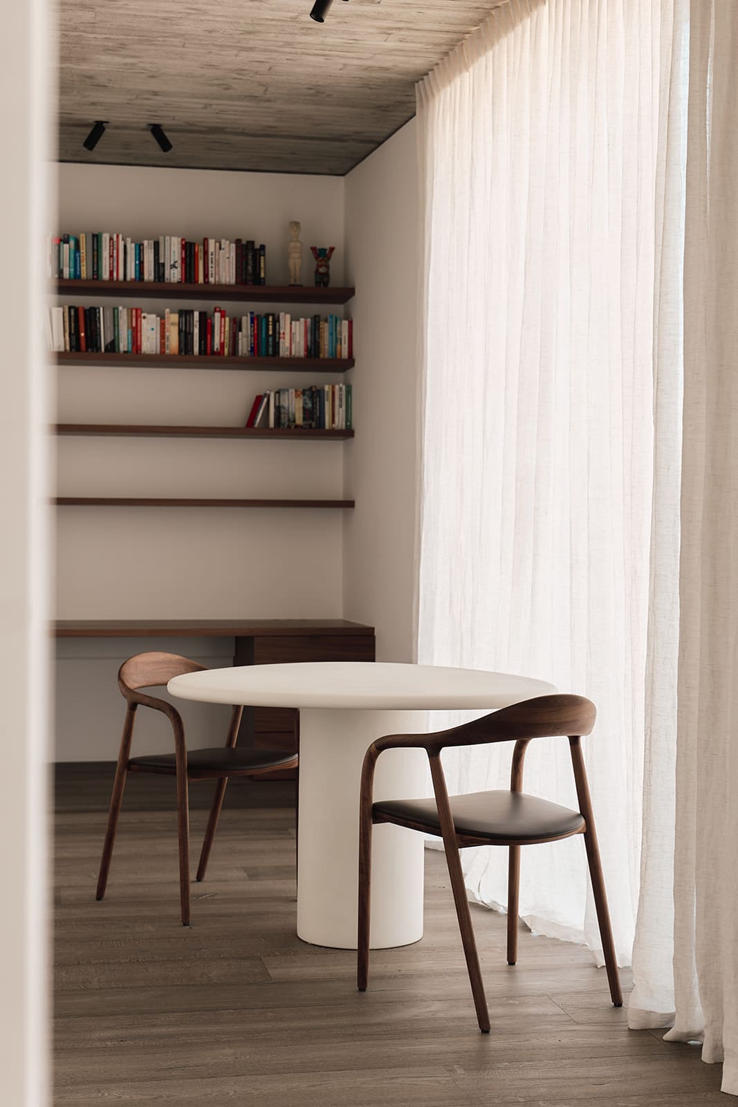 Een ronde, witte mortex tafel in een leeshoek met boeken in de achtergrond
